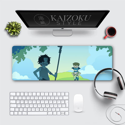 A clean desk setup featuring a custom desk mat with chibi-style artwork of Ace and Sabo from the anime One Piece. The mat shows Ace holding a staff and Sabo wearing goggles, standing under a tree with a bright blue sky and grassy hills in the background.