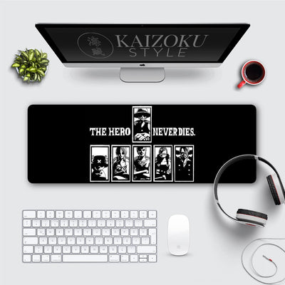 A desk mat featuring a bold black-and-white design with the phrase "The Hero Never Dies" at the center. Below it are silhouettes of iconic One Piece characters, including Luffy, Zoro, Nami, and others, framed in individual panels. The minimalist artwork emphasizes the enduring spirit of the crew.